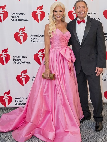 Couple in formal wear standing in front of American Heart Association step and repeat banner.